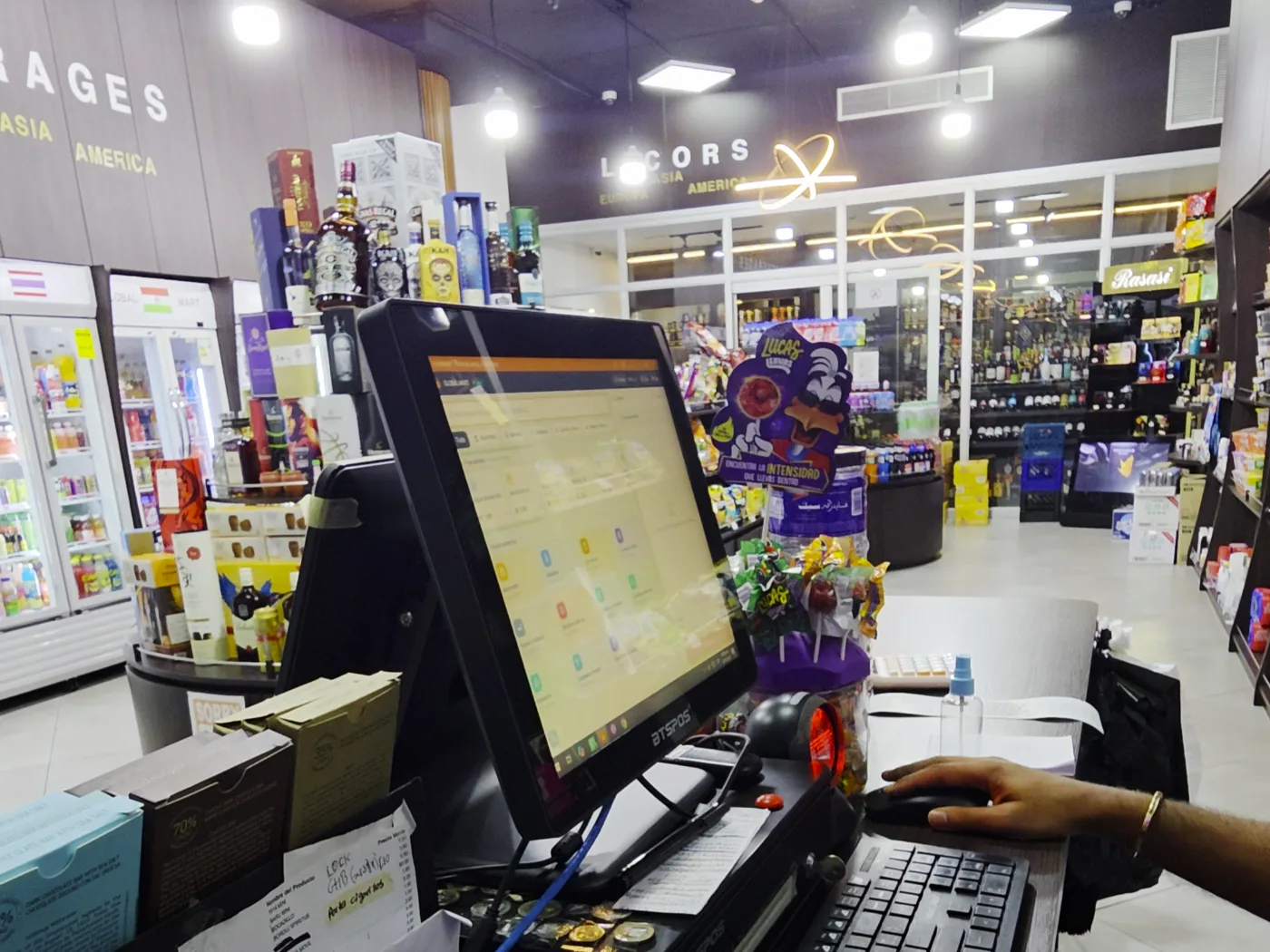 Terminal con HUB Market en la caja de Global Mart, con las góndolas de licores y perfumería al fondo