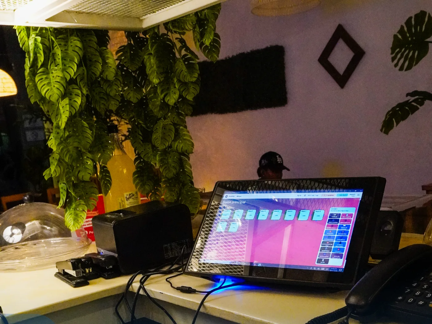 Monitor en el mostrador de un restaurante mostrando el mapa de mesas del salón principal, junto a una impresora y un teléfono.